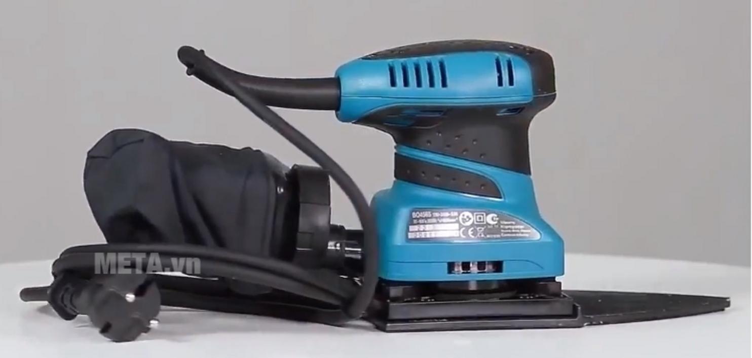 Action shot: Makita BO4565 sanding a wooden panel leaving an even, smooth finish; motion blur minimal, focus on surface texture.
