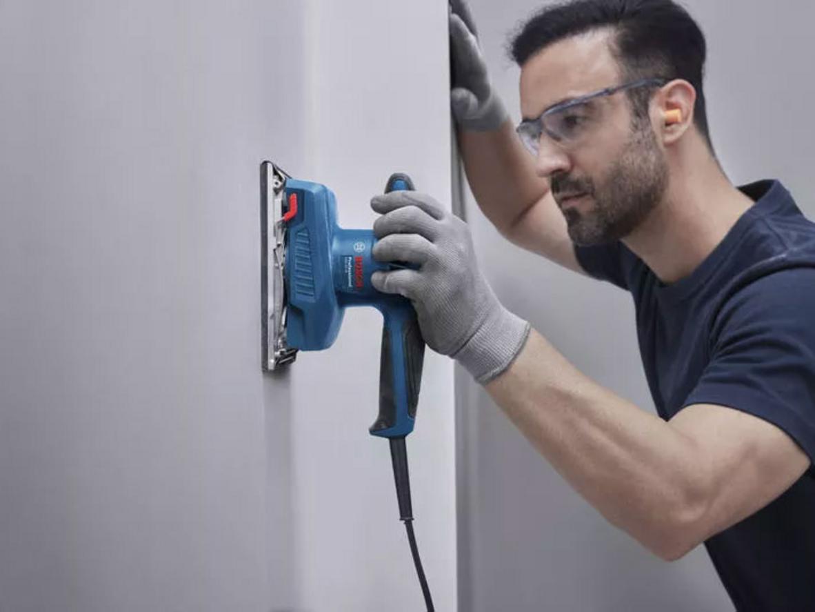 Hiệu suất mạnh mẽ cho hoàn thiện nhanh (200W) - Bosch GSS 20-18 Ảnh minh họa: máy đang chà miếng gỗ trên bàn làm việc bằng gỗ, bề mặt mịn sau khi chà; imagePrompt: Close-up of sander working on wood surface showing smooth finish.
