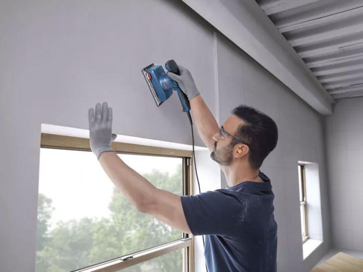 Hiệu suất mạnh mẽ cho hoàn thiện nhanh (200W) - Bosch GSS 20-18 Ảnh minh họa: máy đang chà miếng gỗ trên bàn làm việc bằng gỗ, bề mặt mịn sau khi chà; imagePrompt: Close-up of sander working on wood surface showing smooth finish.