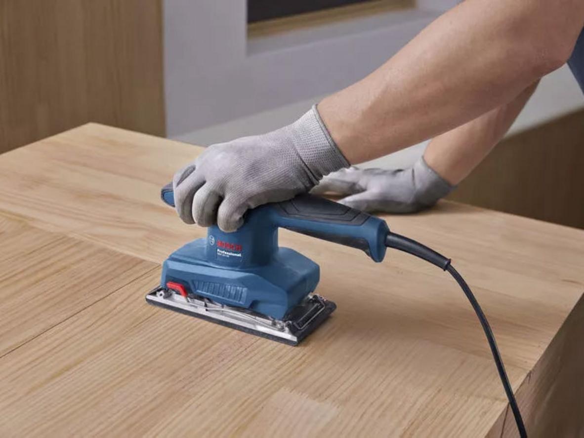 Nhẹ và rung thấp — tiện lợi cho công việc dài; imagePrompt: Carpenter using the sander comfortably with one hand, workshop background.