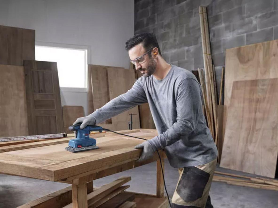 Nhẹ và rung thấp — tiện lợi cho công việc dài; imagePrompt: Carpenter using the sander comfortably with one hand, workshop background.